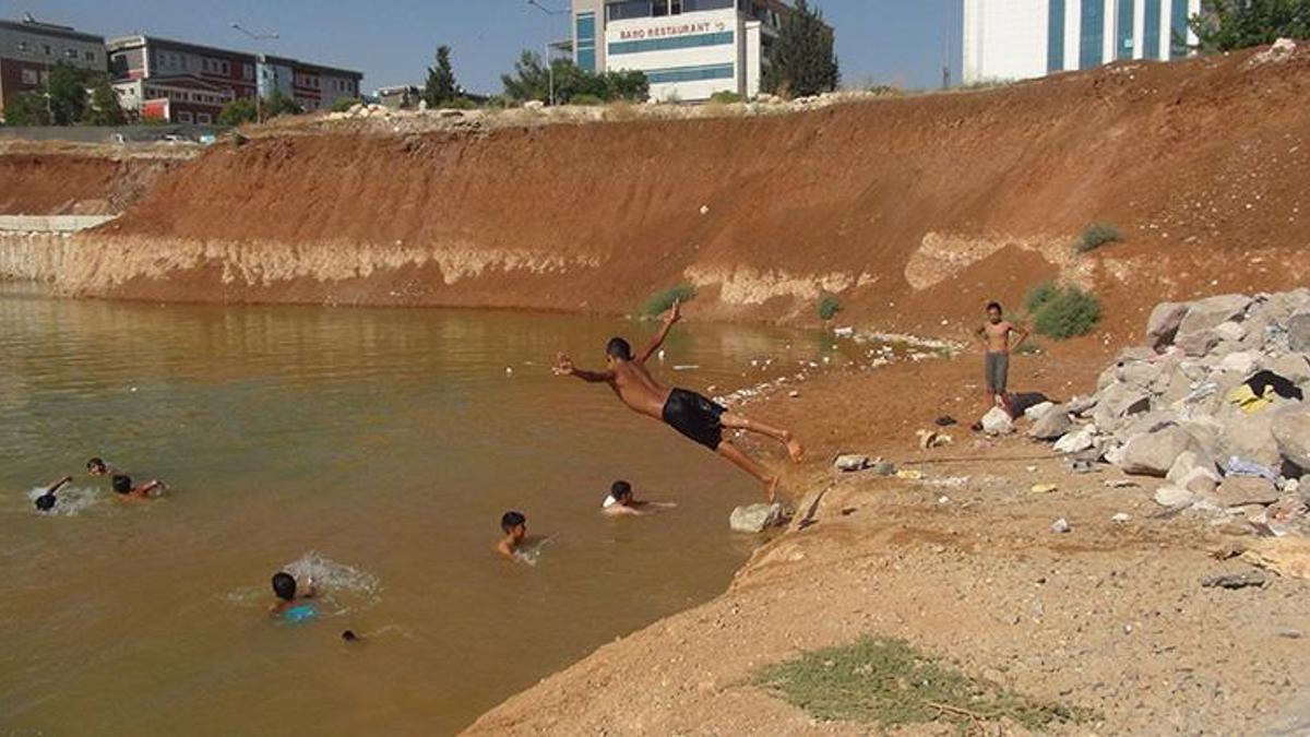 Çocuklar, inşaat temelini dolduran kirli suda yüzüyor